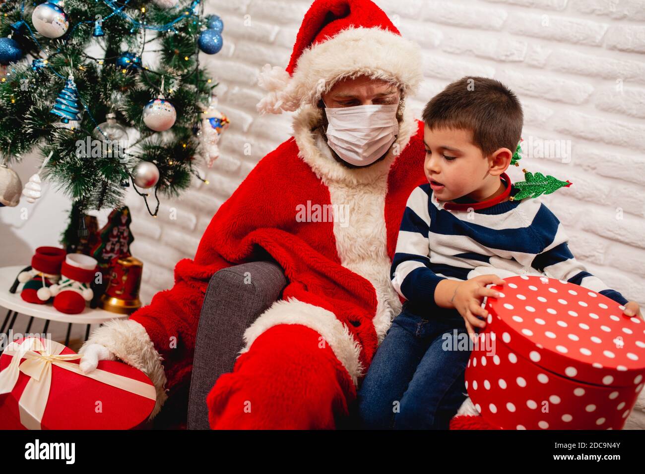 A 5 Year Old Boy Sitting In Santa's Lap With A Face Mask And Watching A  Xmas Gift Next To A Christmas Tree. New Year And Christmas Pandemic Covid - 19 Stock Photo - Alamy
