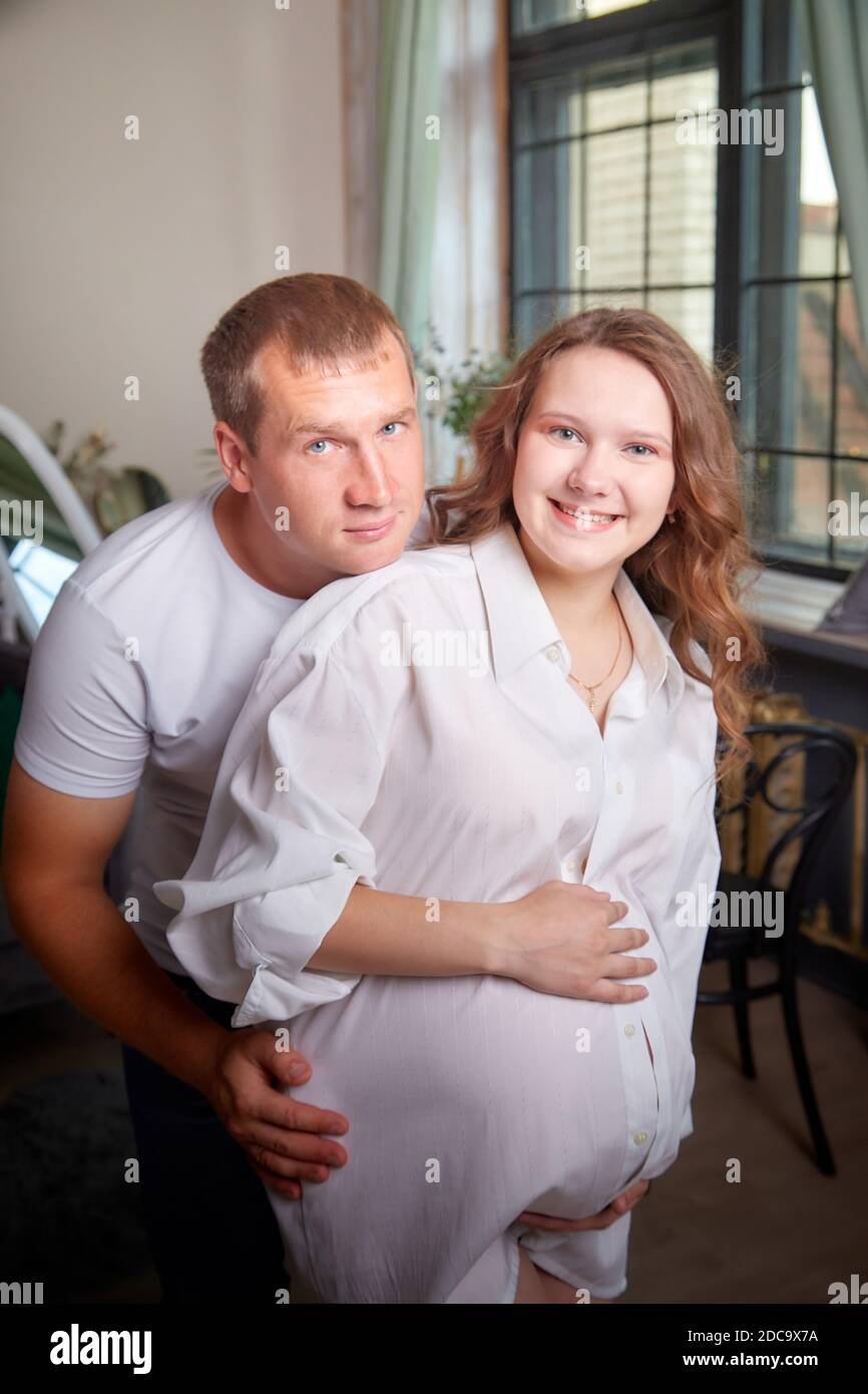Cute couple including a pregnant woman and a caring man in the living room together. Beautiful pregnant future mother and father at home Stock Photo
