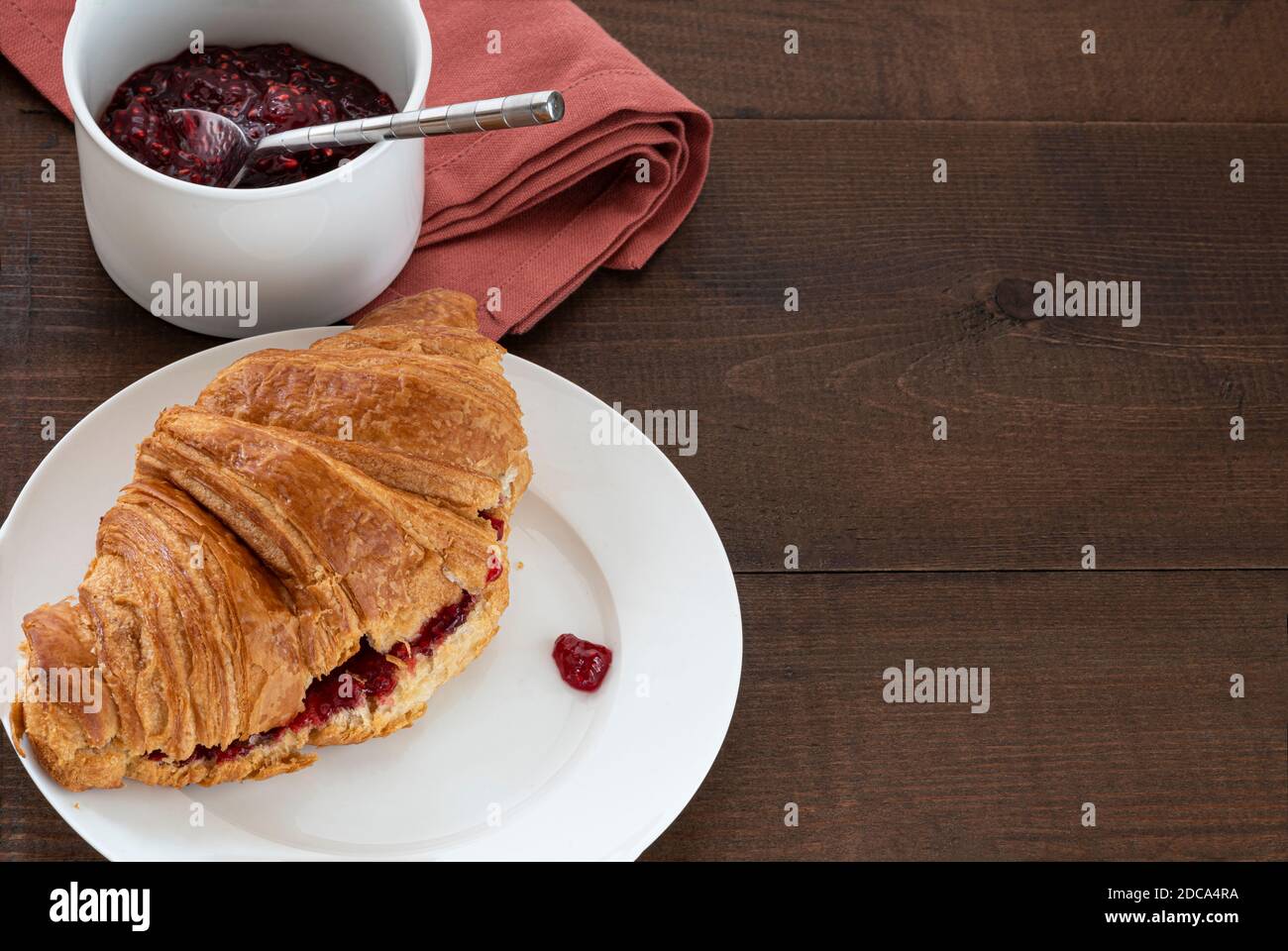 Jam filled croissant  on a plate, with a pot of preserve. Placed on a wooden table top. Stock Photo