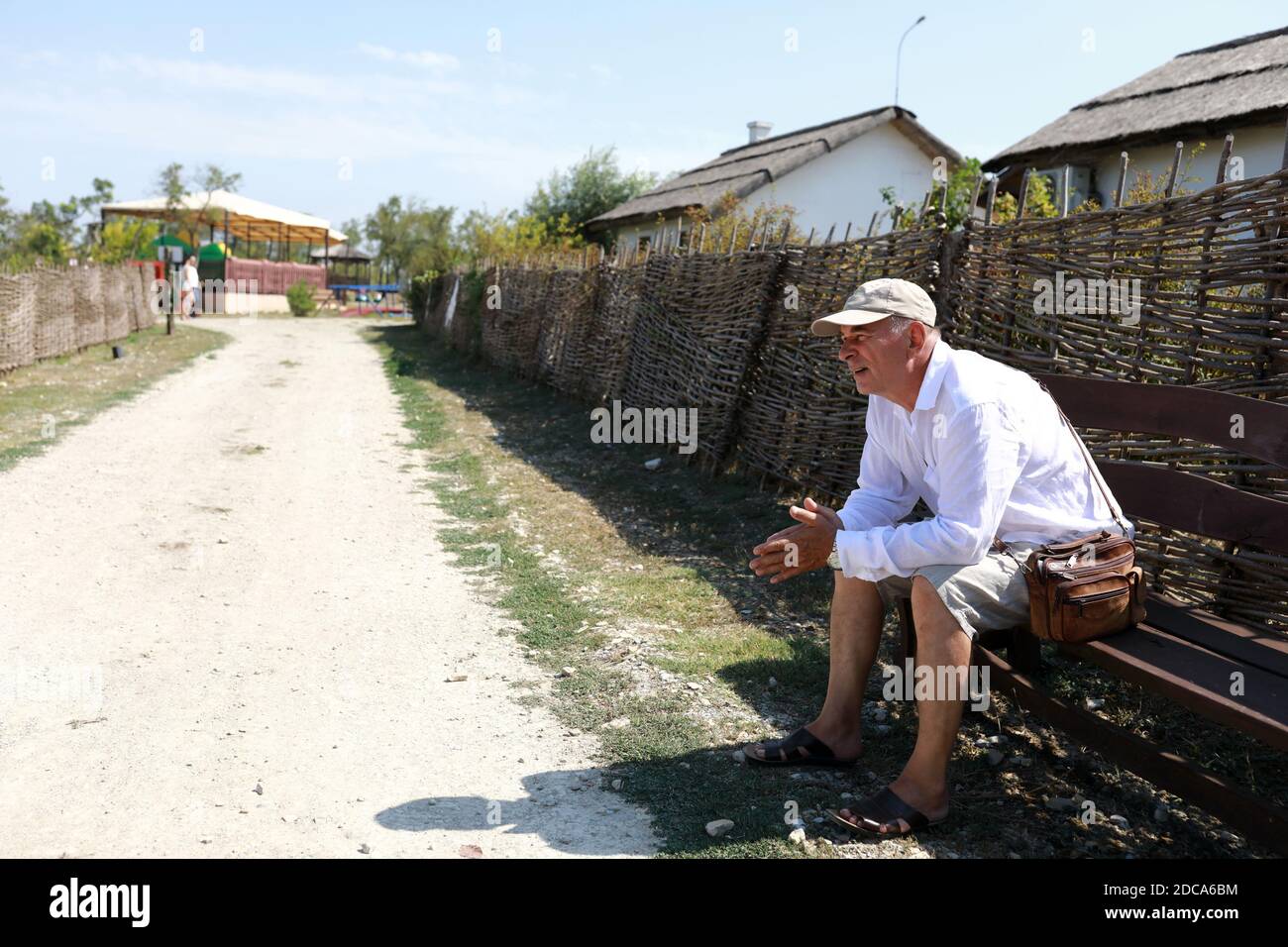 Elderly man sitting on bench in village Stock Photo - Alamy