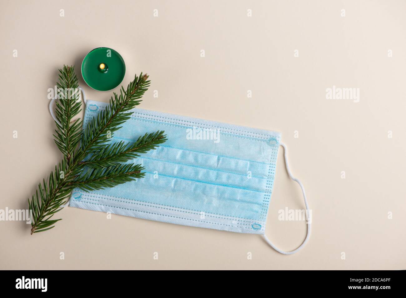 Medical face protective mask, candle and fir twig on a light background. Isolated, top view, flat lay. Stock Photo
