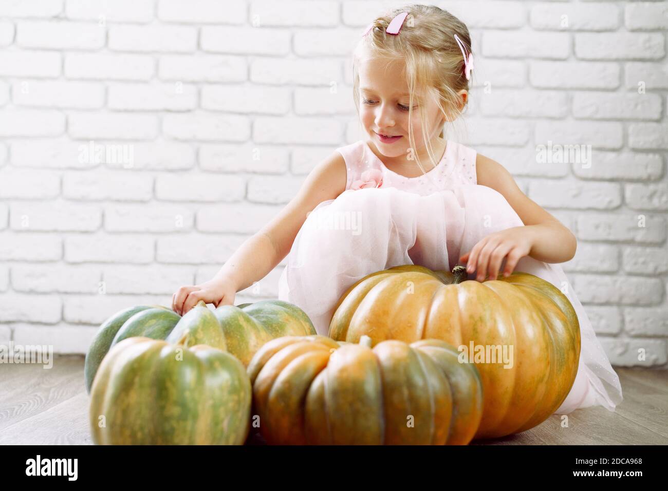 Little girl in pink dress sitting on wooden floor and playing with pile ...