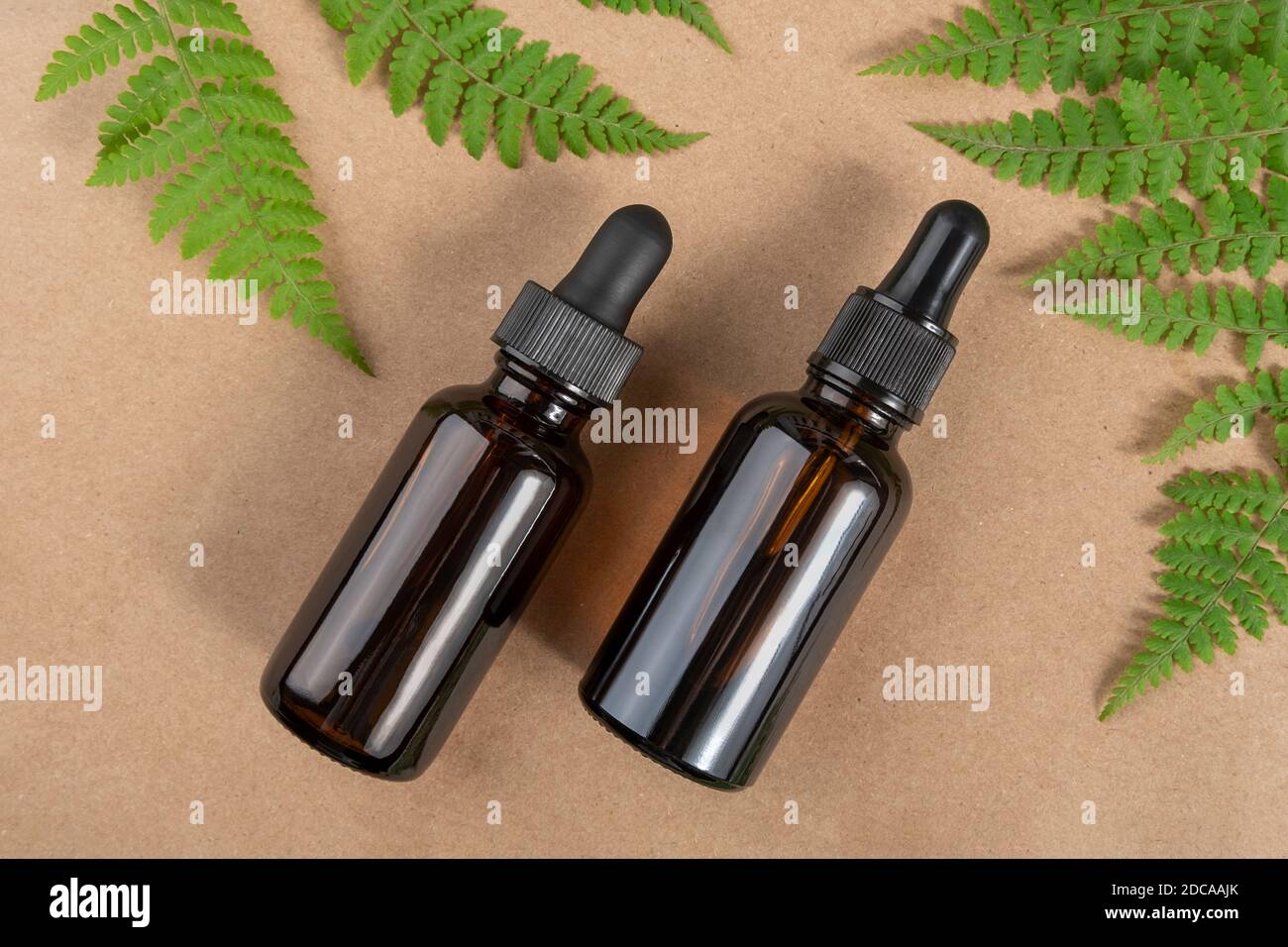 Two brown glass bottles with serum, essential oil or other cosmetic product and green fern leaves on craft beige background. Natural Organic Spa Cosme Stock Photo