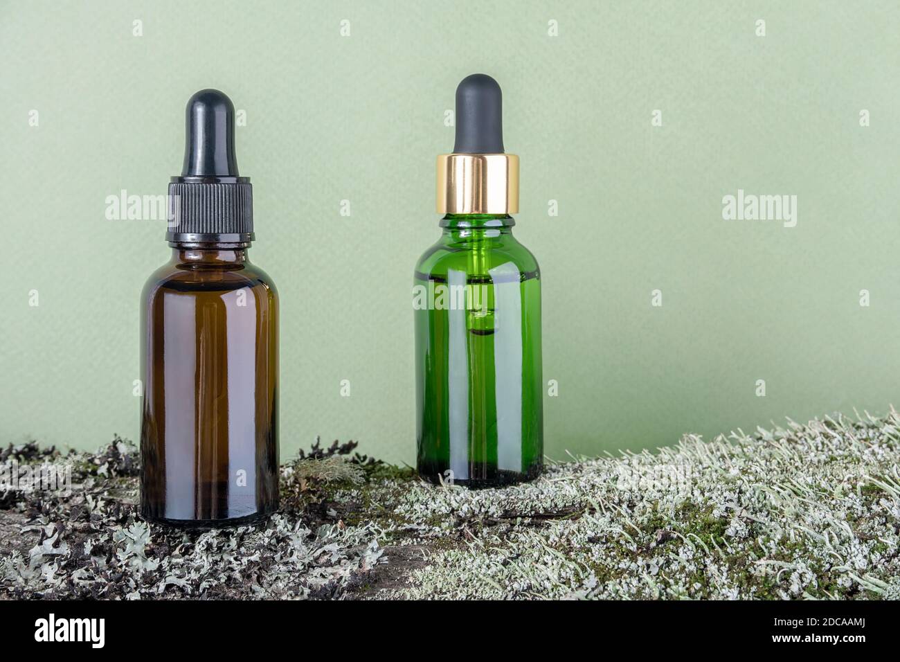 Two brown, green glass bottles with serum, essential oil or other cosmetic product on tree bark covered with moss against green background. Natural Or Stock Photo
