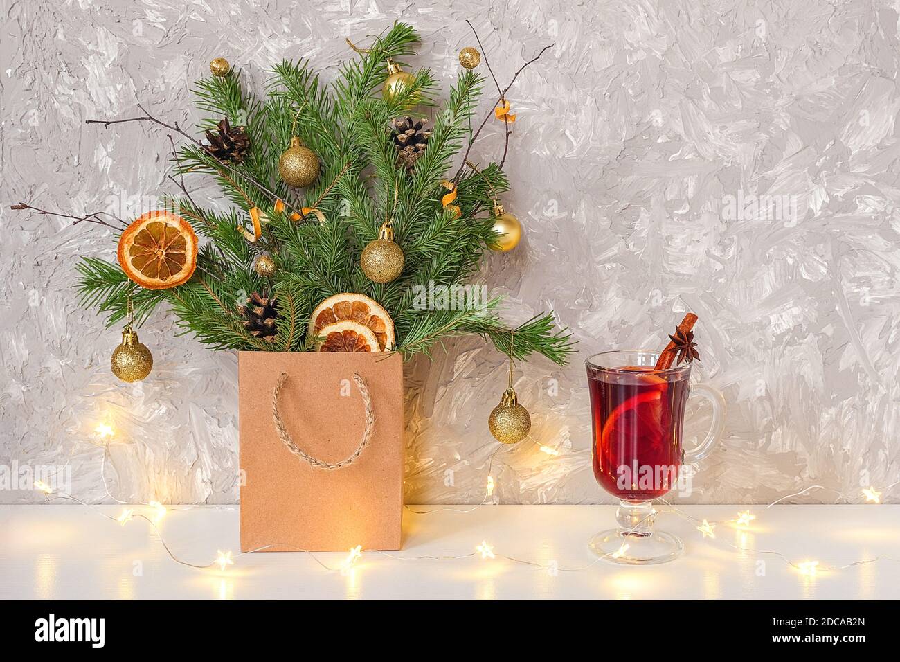 Christmas tree decorated golden balls, cones in craft package, lights garland and glass of hot mulled wine with spices on table. Xmas or New Year, win Stock Photo