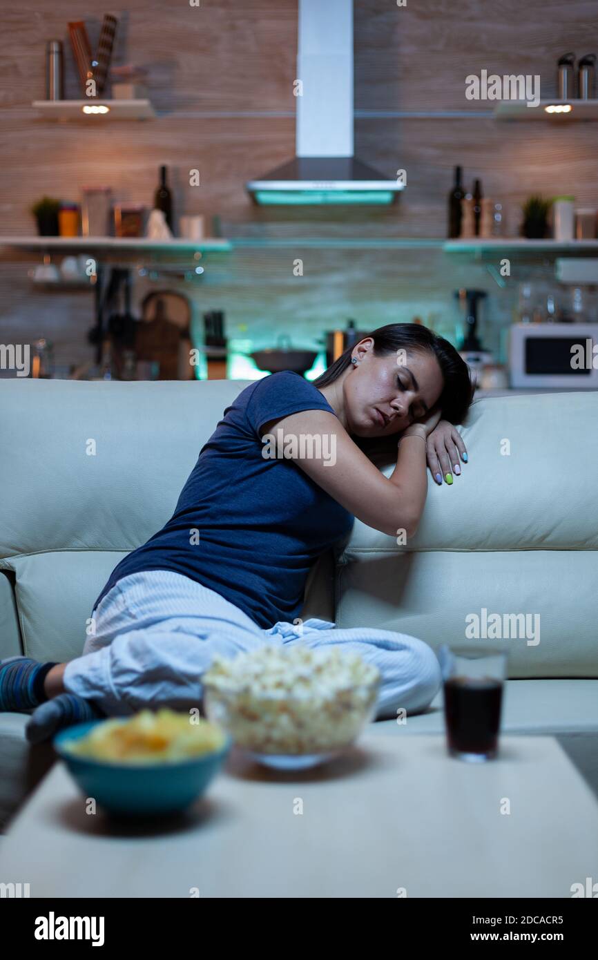 Tired lonely woman sleeping on sofa in living room while watching film
