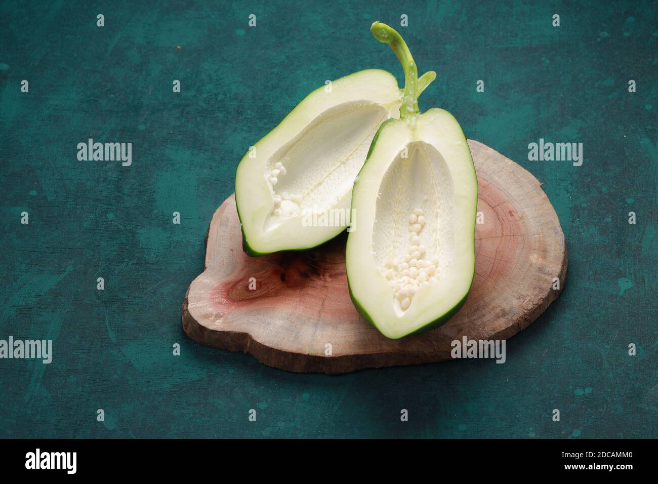 Fresh green papaya ,splitted into two pieces and arranged on a wooden piece with dark green background Stock Photo