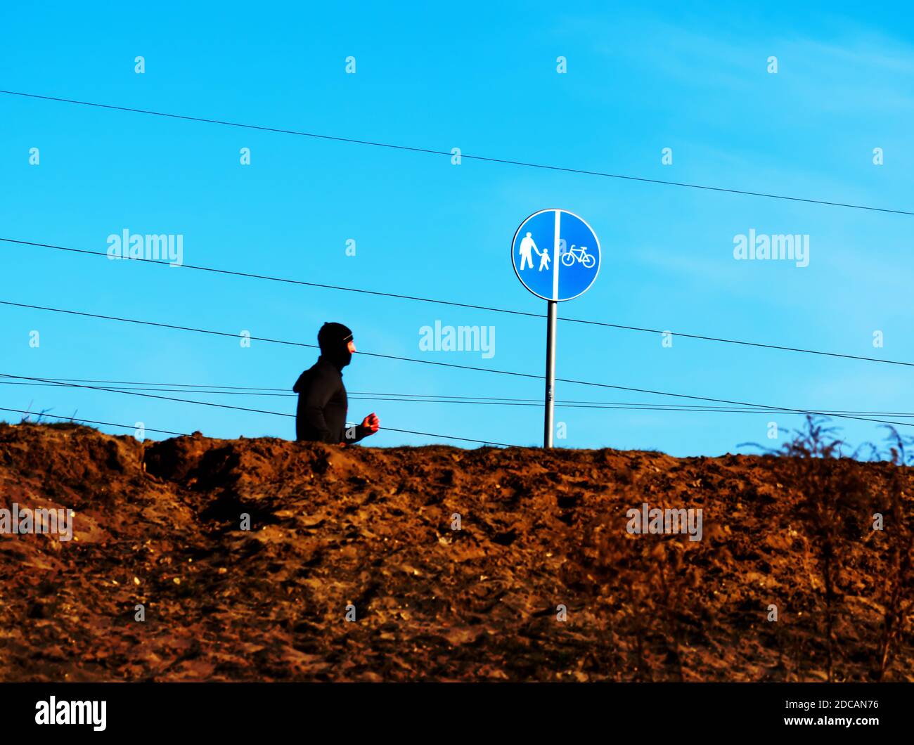 Man running in balaclava with power lines and clear blue sky in