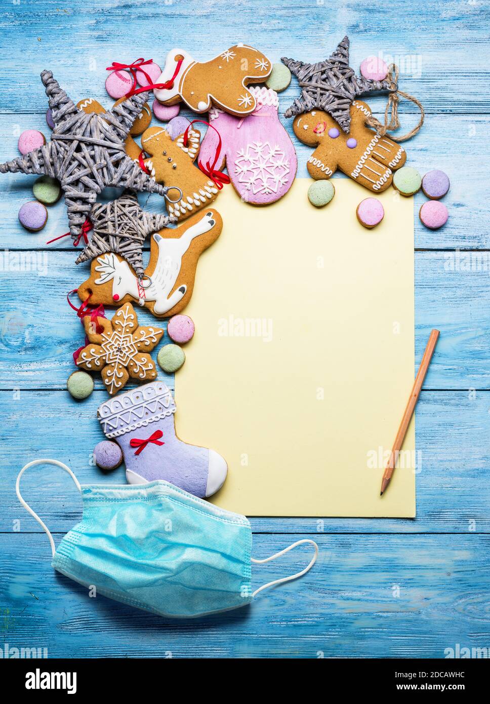 Empty Santa letter with Christmas traditional ginger cookies around it on wooden background. Medical mask is a permanent attribute of people. Stock Photo