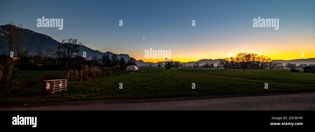 Sunset in the valley of Rhein. Sonnenuntergang im Rheintal. Säntis, die Schweizer und Vorarlberger Berge im Hintergrund. junger Baum steht mit Pfahl Stock Photo