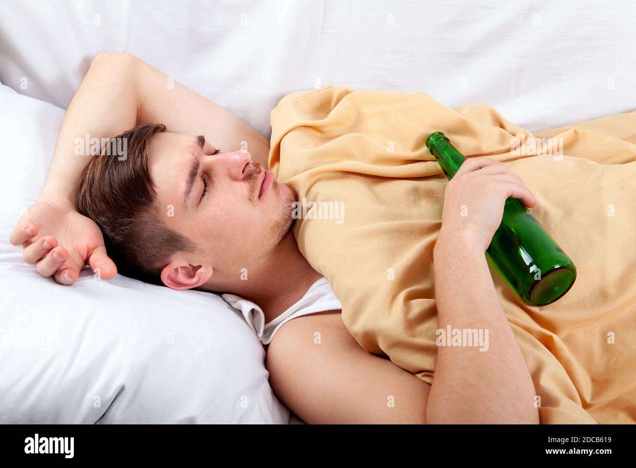 Young Man sleep with a Beer Bottle in the Bed at the Home Stock Photo