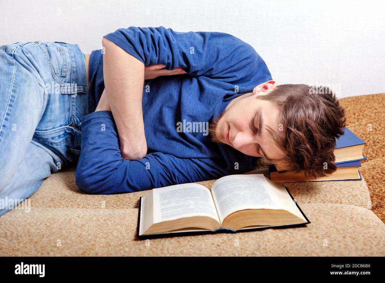 Tired Young Man sleep on the Sofa with the Books Stock Photo