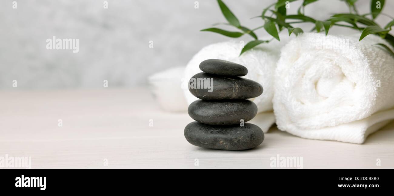 spa and wellness center - stack of massage stones and towels with green plant on white wooden table. banner copy space Stock Photo