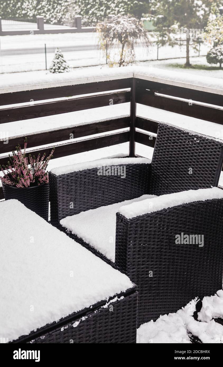 Close up view of snowy synthetic plastic rattan and glass garden furniture on cold winter day. Garden furniture maintenance concept. Stock Photo