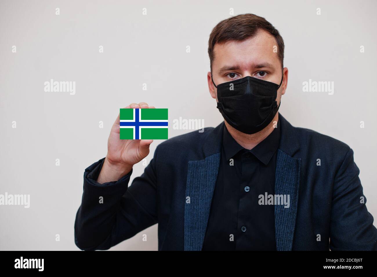 Man wear black formal and protect face mask, hold South Uist flag card isolated on white background.  United Kingdom territories of Scotland coronavir Stock Photo