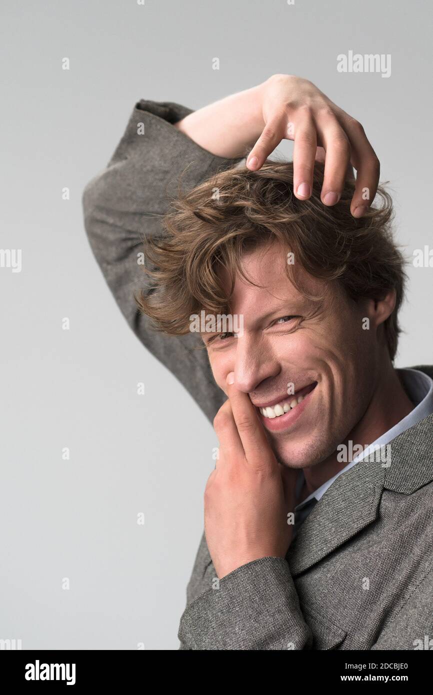 Young handsome man smiling positively and confidently posing with hands on his face and head, looking satisfied, friendly and happy against grey Stock Photo
