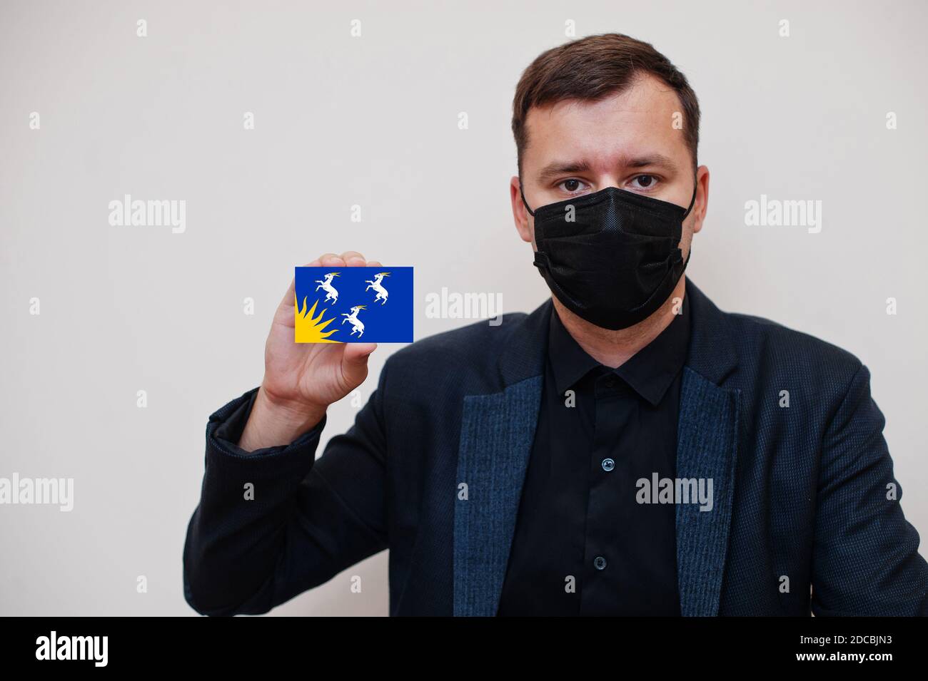 Man wear black formal and protect face mask, hold Merionethshire flag card isolated on white background. United Kingdom counties of Wales coronavirus Stock Photo