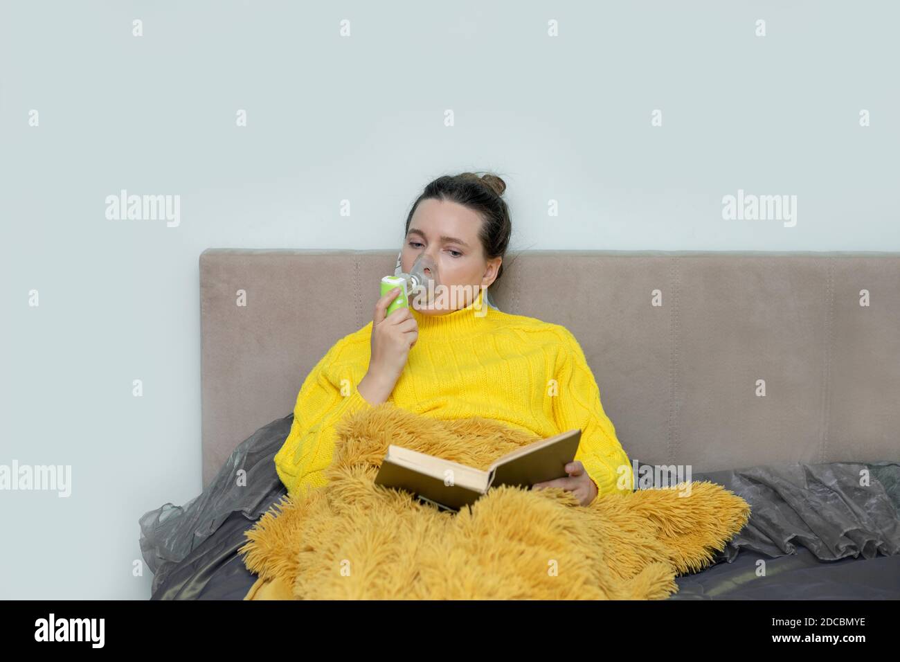 Woman reading book in bed, doing inhalation with a nebulizer at home, stay isolation for self quarantine. Concept home quarantine, prevention COVID-19 Stock Photo