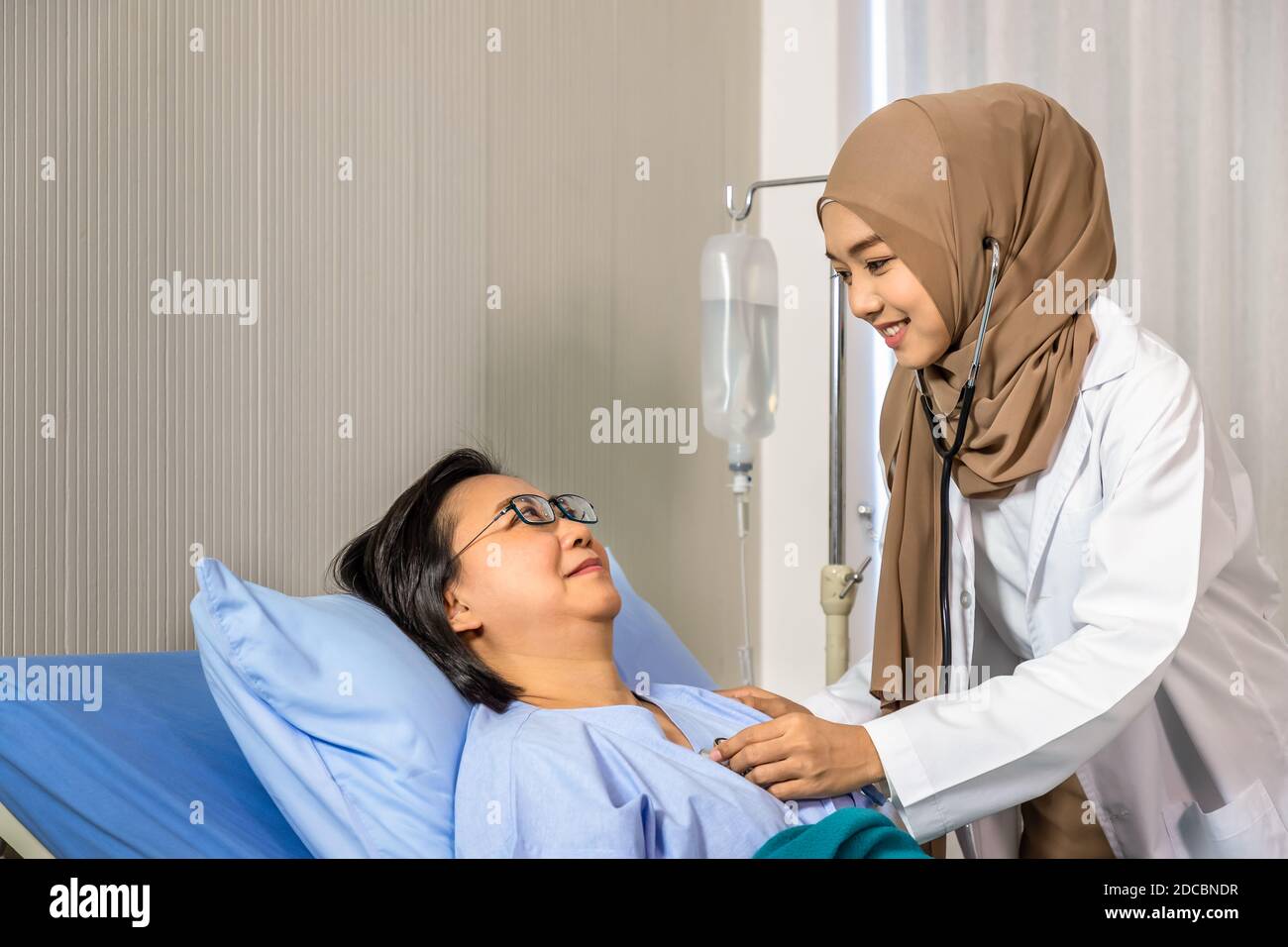 Muslim female woman medical doctor using stethoscope to listen to heartbeat, patient lying on bed Stock Photo