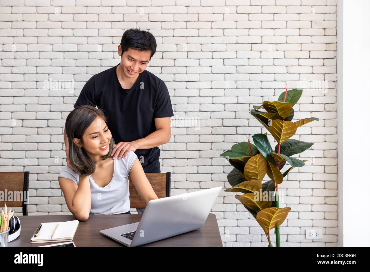 Asian man husband motivate support wife woman freelancer working at home, sitting at desk dining table in living room Stock Photo