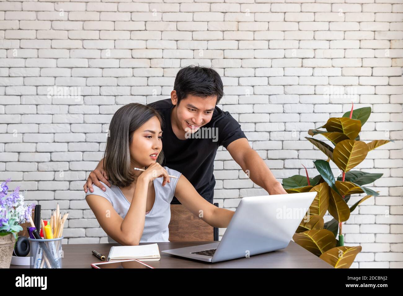 Asian man husband motivate advice wife woman freelancer working at home, sitting at desk dining table in living room Stock Photo