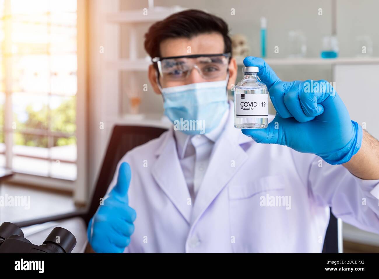 Arab Middle East male researcher scientist doctor holding Corona Virus Covid-19 vaccine with thumb up in laboratory, selective focus Stock Photo