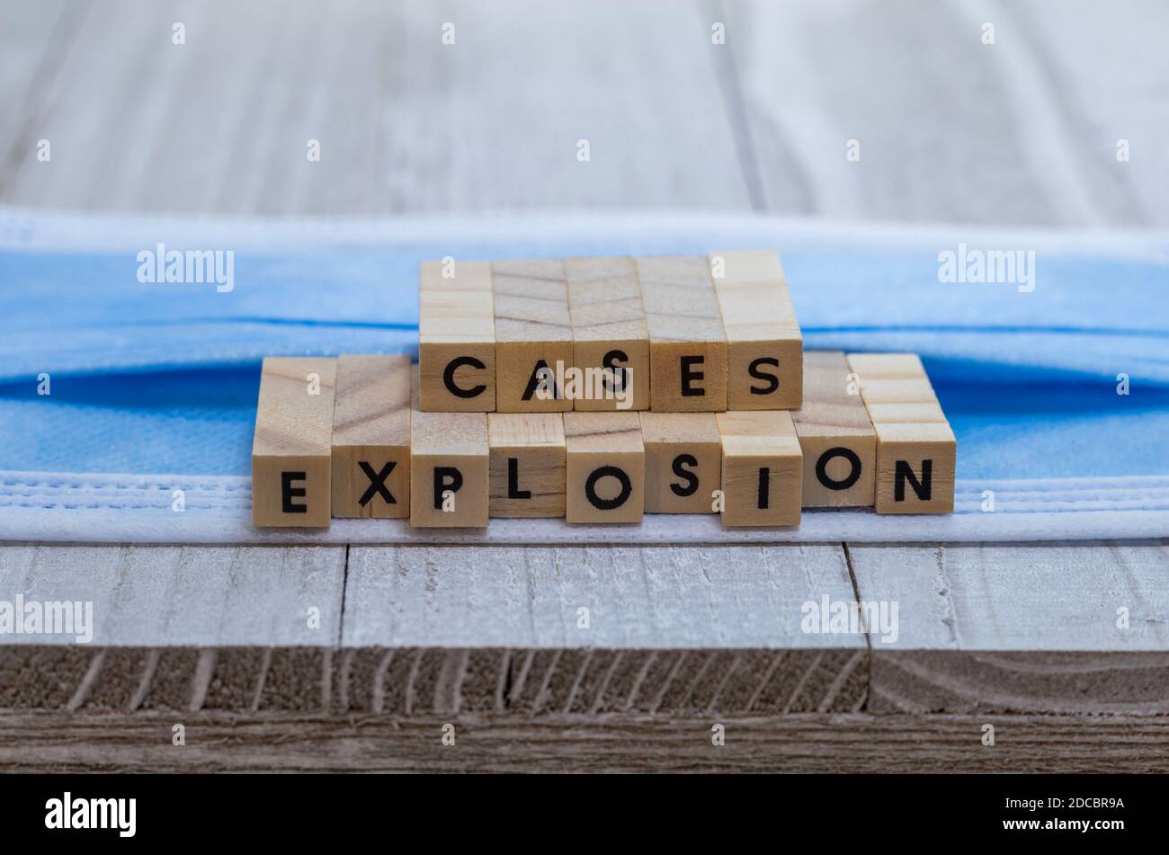 EXPLOSION of cases on face mask covid pandemic alert concept wood block letters on board cool blue tone background Stock Photo
