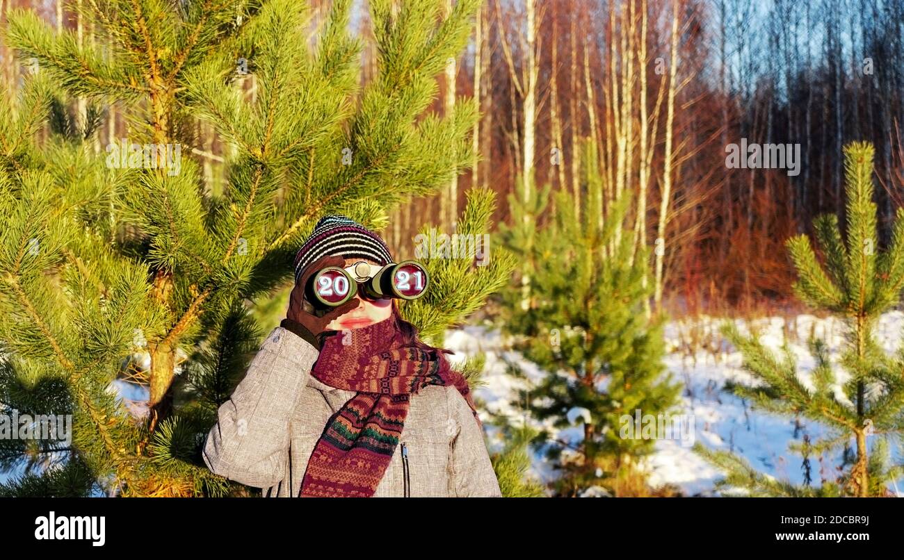upcoming new year 2021 and christmas concept. Young woman in knitted hat and scarf looking through binoculars with numbers 2021 in eyepieces in winter Stock Photo