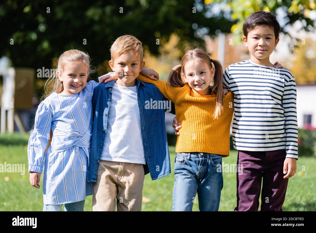 Multicultural kids smiling at camera while hugging in park Stock Photo