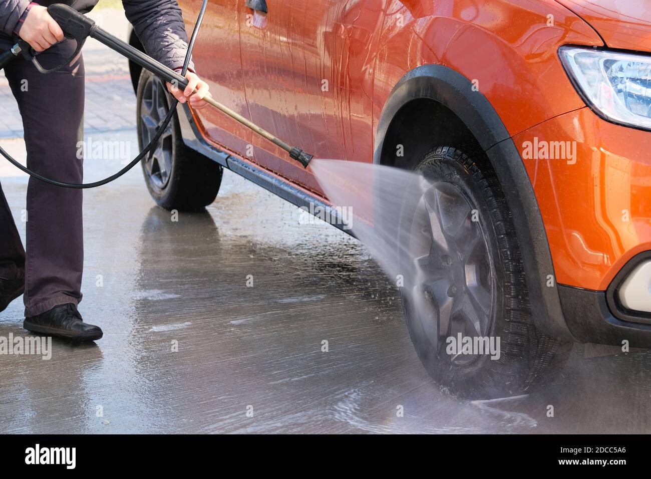 Man washes his orange car at car wash. Cleaning with water at self-service car wash. Soapy water runs down. Stock Photo