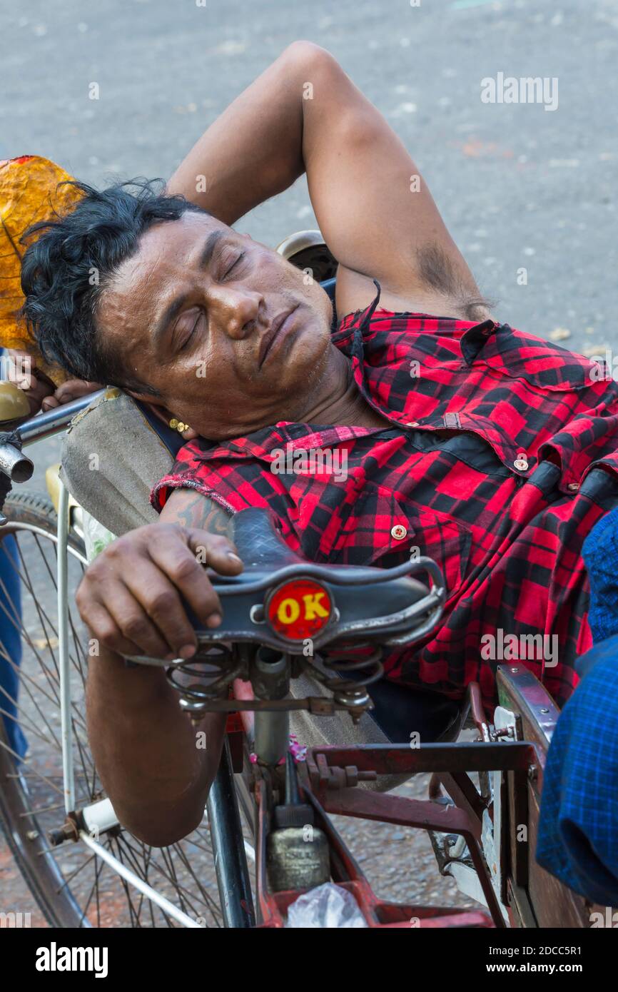Daily life in Myanmar - man lying against bike with eyes closed holding tobacco leaf at Yangon, Myanmar (Burma), Asia in February Stock Photo