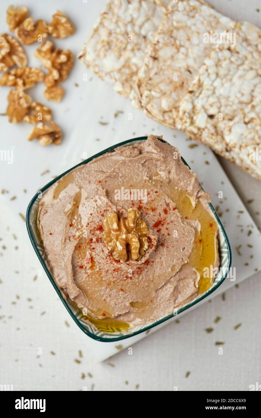 high angle view of a bowl with an appetizing hummus, made with chickpea, walnut and rosemary, on a table, next to some puffed rice cakes Stock Photo