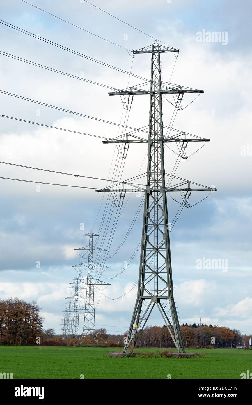 Row of electricity pylons with wires against blue sky with clouds Stock Photo
