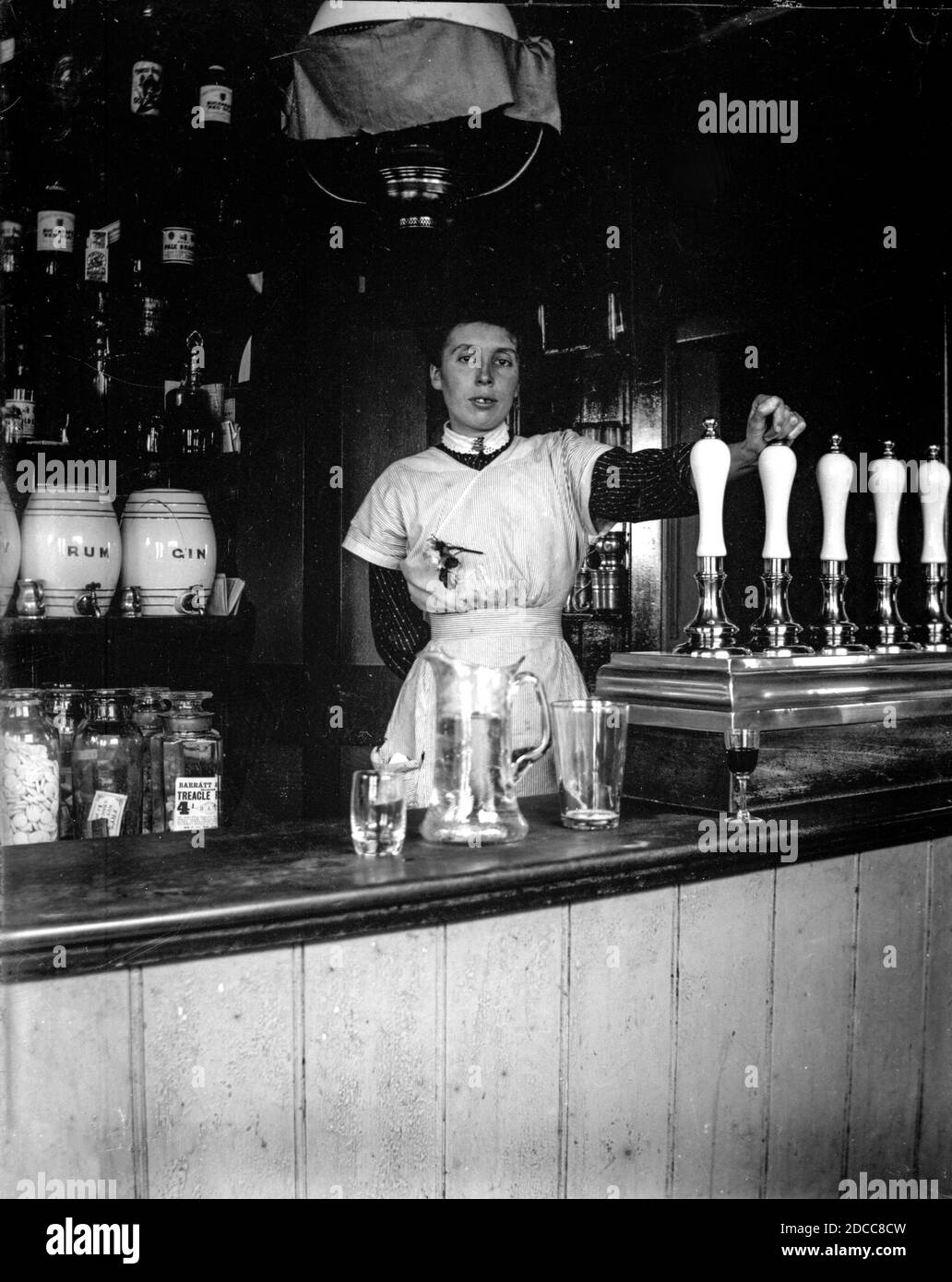 A barmaid leans against the beer pumps in a public house in Victorian London, around 1890 Stock Photo