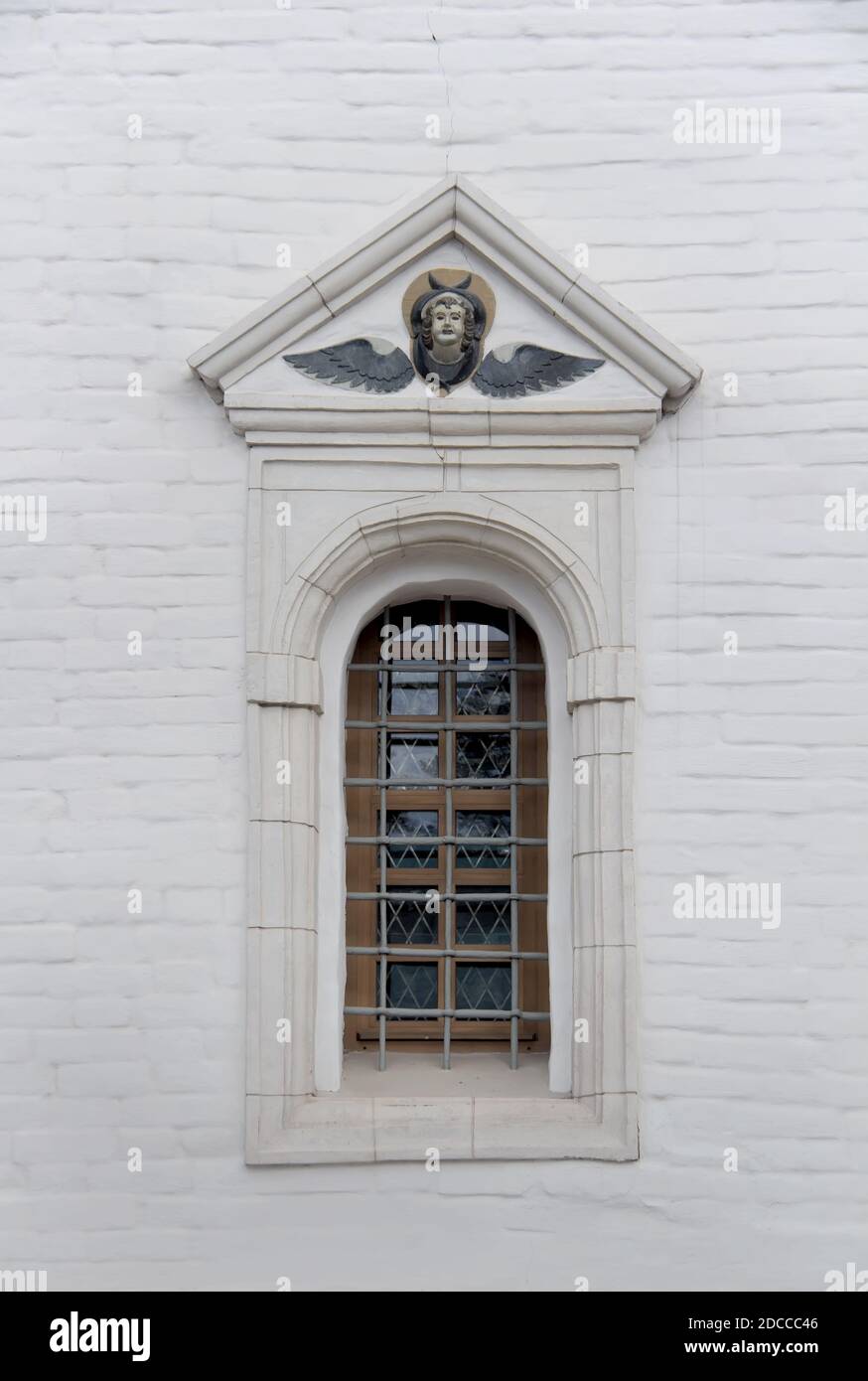 Old arched window with metall lattice and relief on a white brick wall of christian church Stock Photo