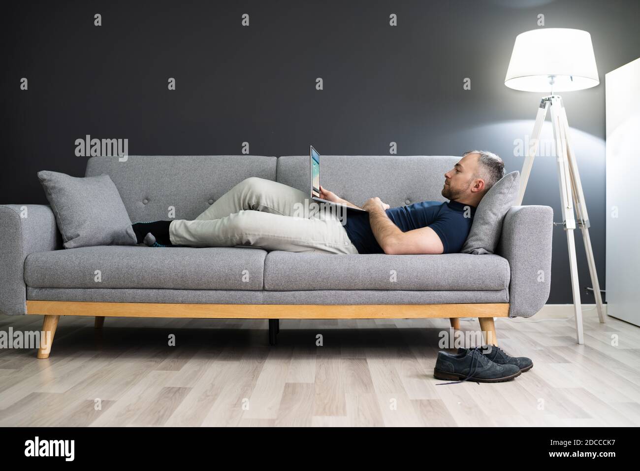 Man Lying In Sofa At Home And Using Laptop Stock Photo