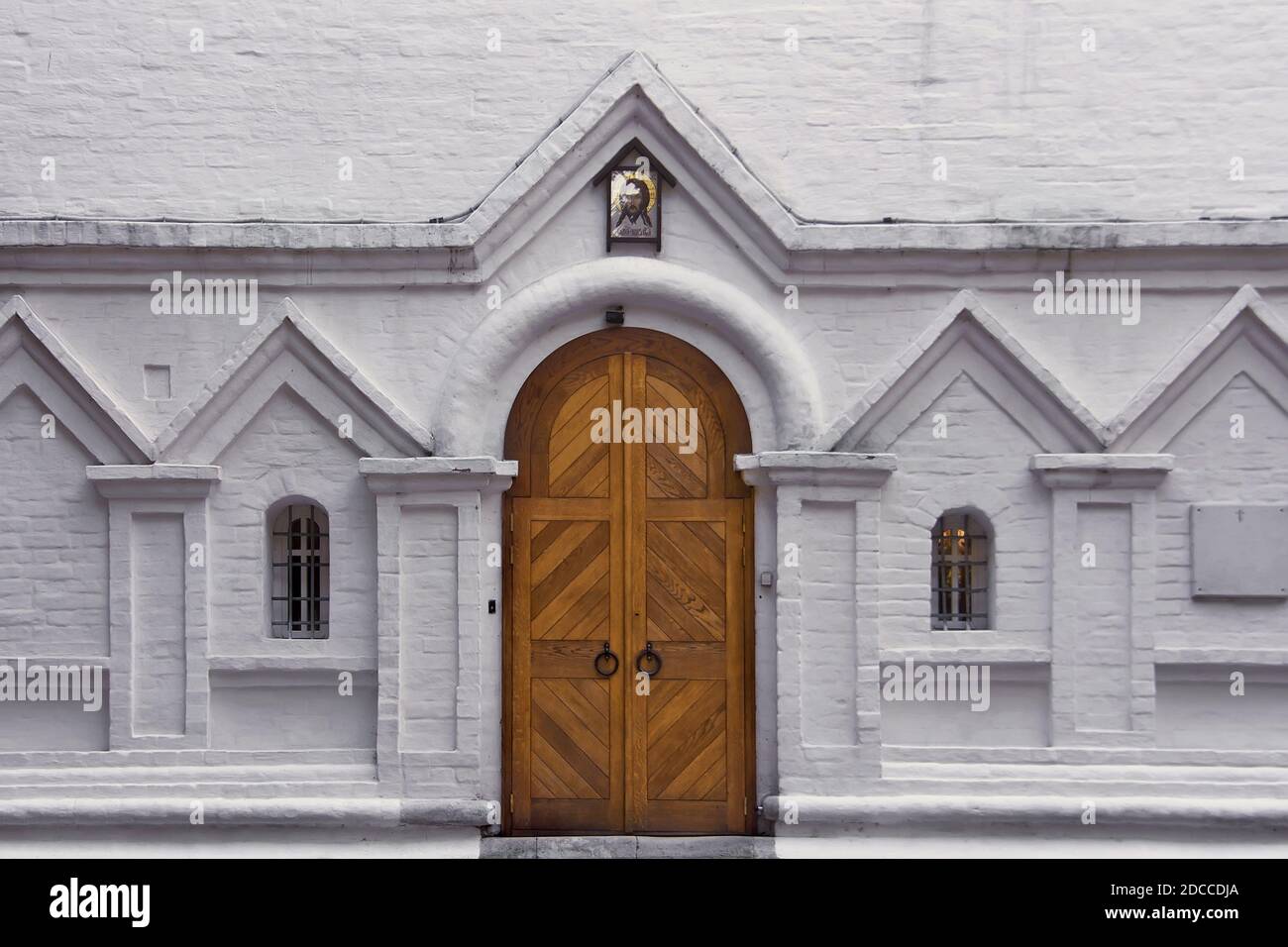 Wooden gate and two arched windows on a white brick wall. Entrance to the old christian church Stock Photo