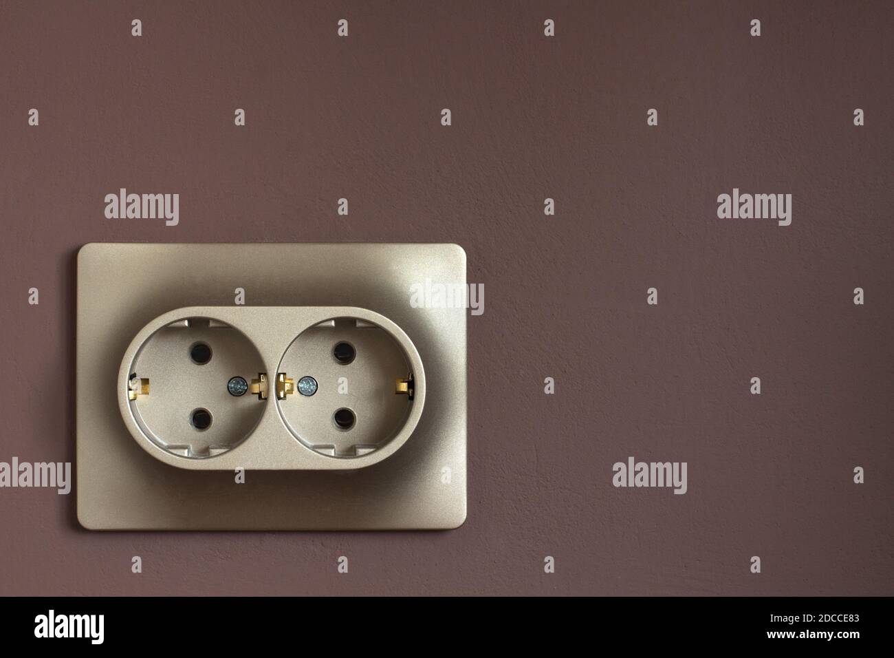 Golden double power socket on a painted brown wall. Standard european electrical connector close-up Stock Photo