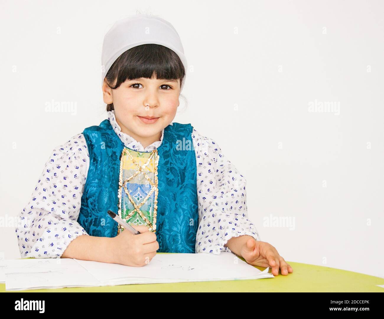 A little girl is sitting at a table, doing a drawing task, smiling and looking at the camera Stock Photo