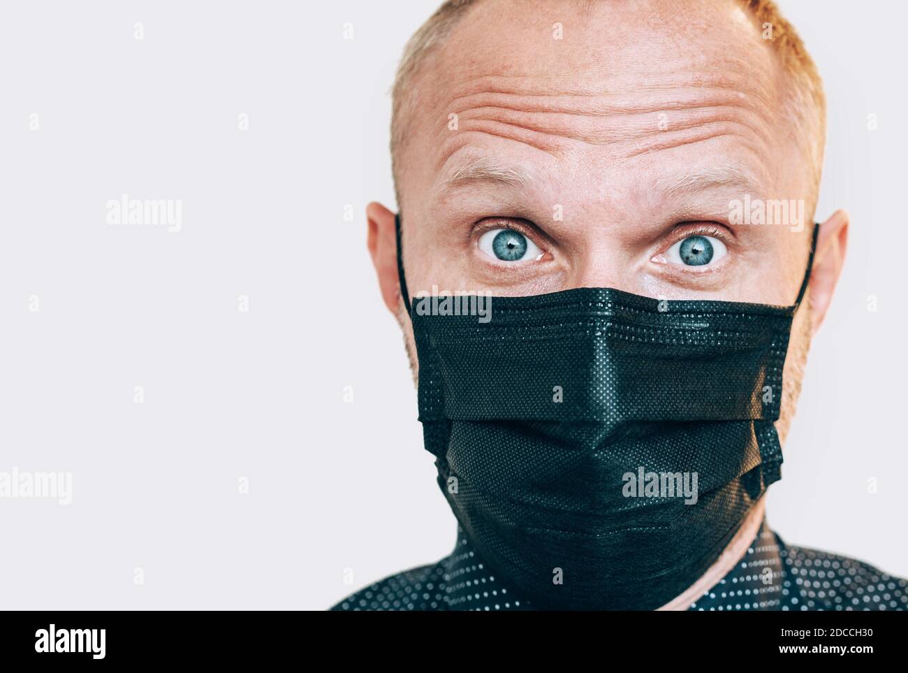 Portrait of surprised man in black facial mask during a COVID-19 world pandemic looking at camera. Self-protection and stop virus spreading measures c Stock Photo