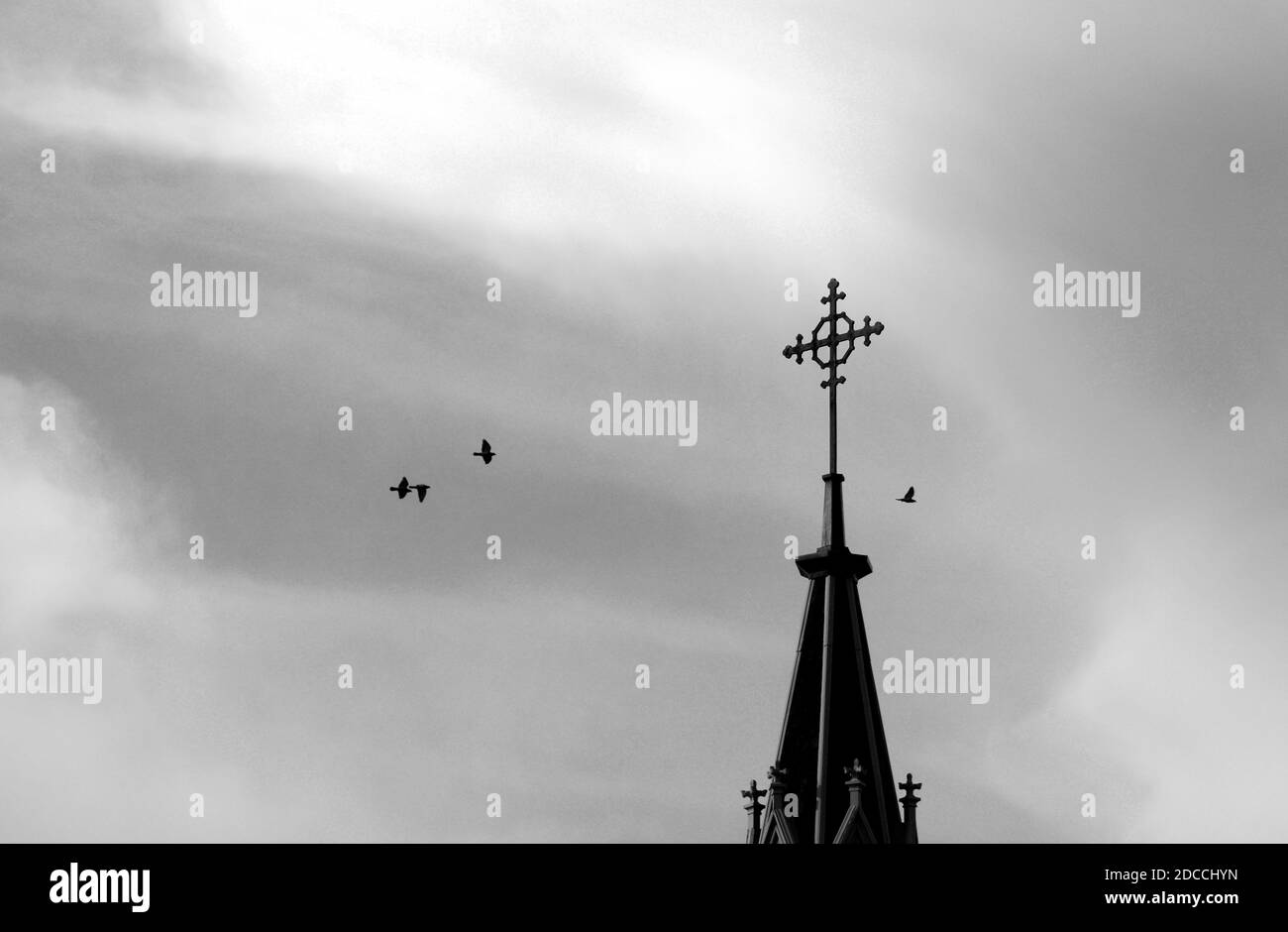 A flock of pigeons circle the Christian cross atop the historic Loretto Chapel in Santa Fe, New Mexico. Stock Photo