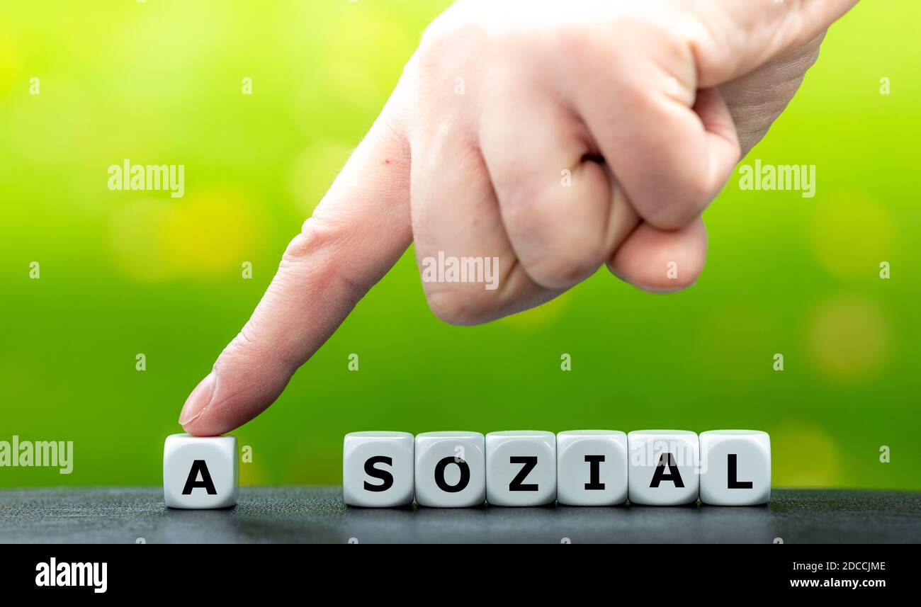 Hand moves a dice and changes the German word 'asozial' (asocial) to 'sozial' (social). Stock Photo