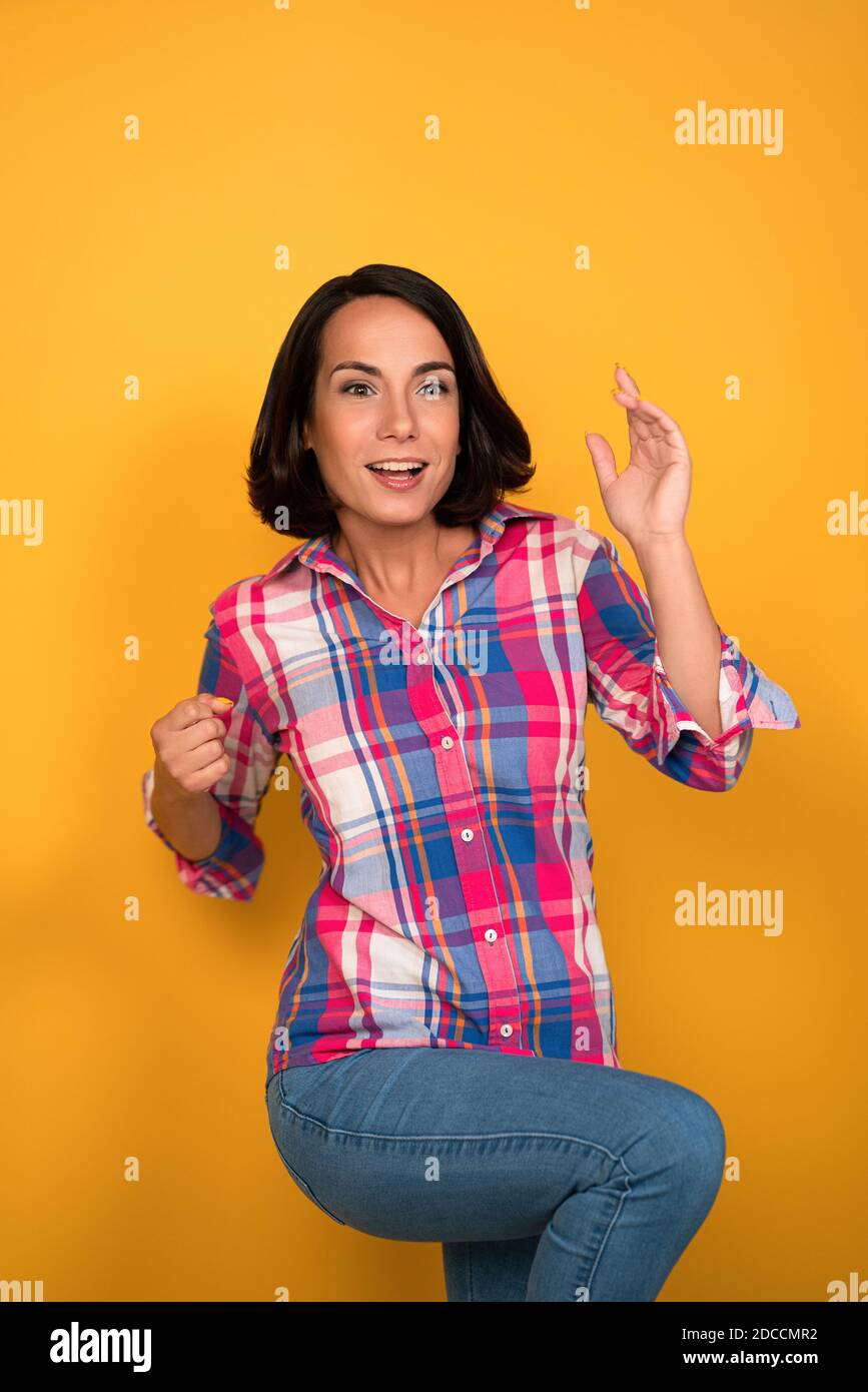 Funny young woman rejoices at lucky win. Fortune concept. Laughing Caucasian brunette wearing jeans. Isolated on yellow background Stock Photo