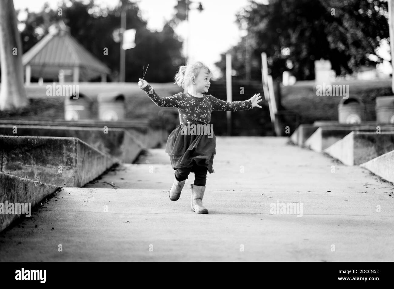 Black and white image of a toddler girl running at the Polliwog Park in Manhattan Beach, CA. Stock Photo