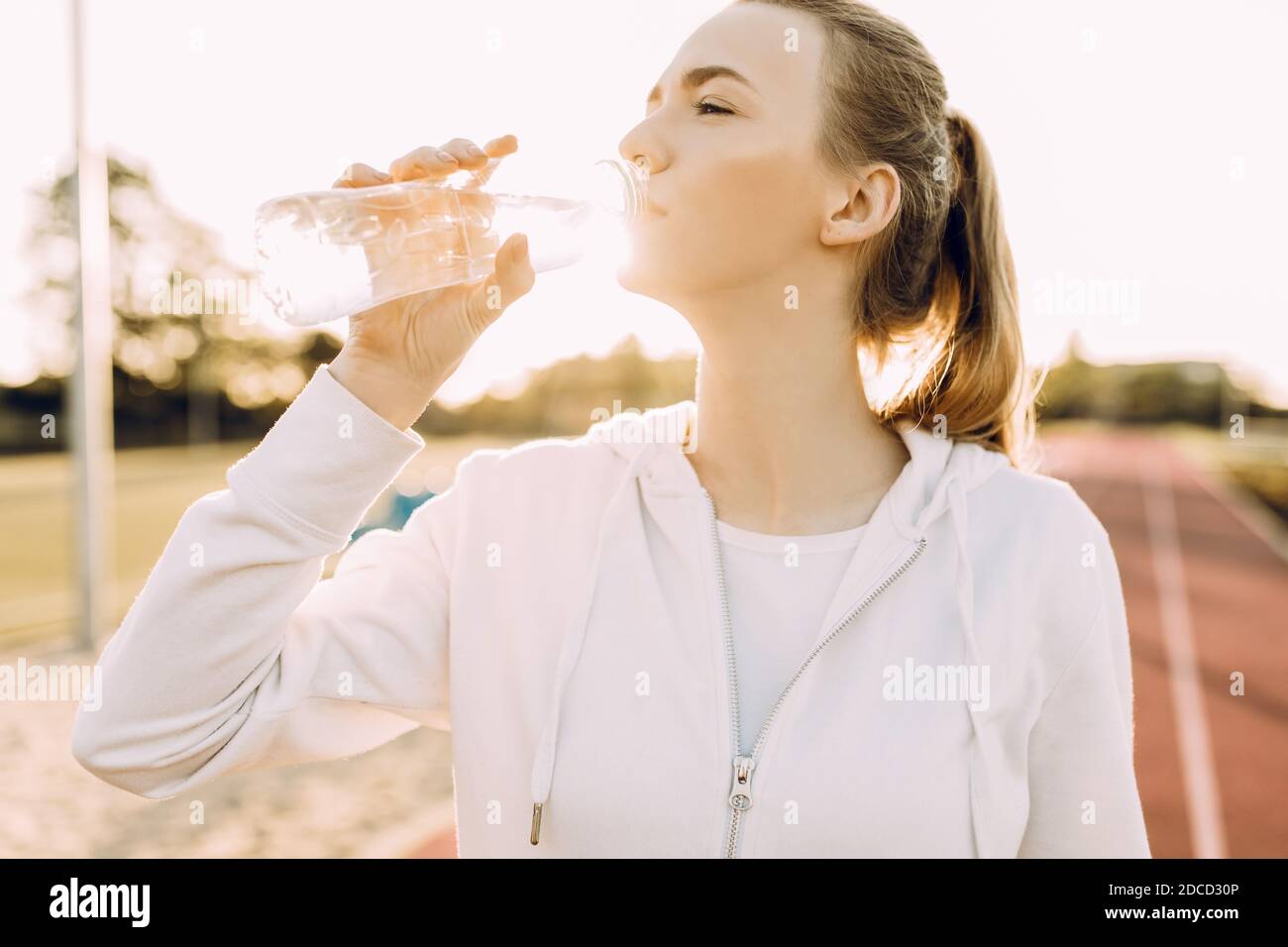 Athletic beautiful runner drinks water from a plastic bottle after