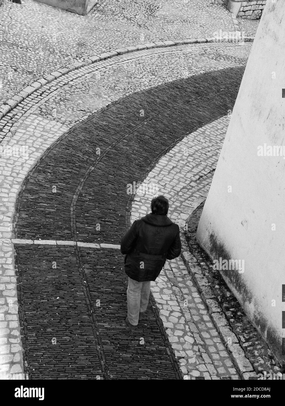 Monochrome, man walking down slope, seen from behind, hands in pockets. High quality photo Stock Photo