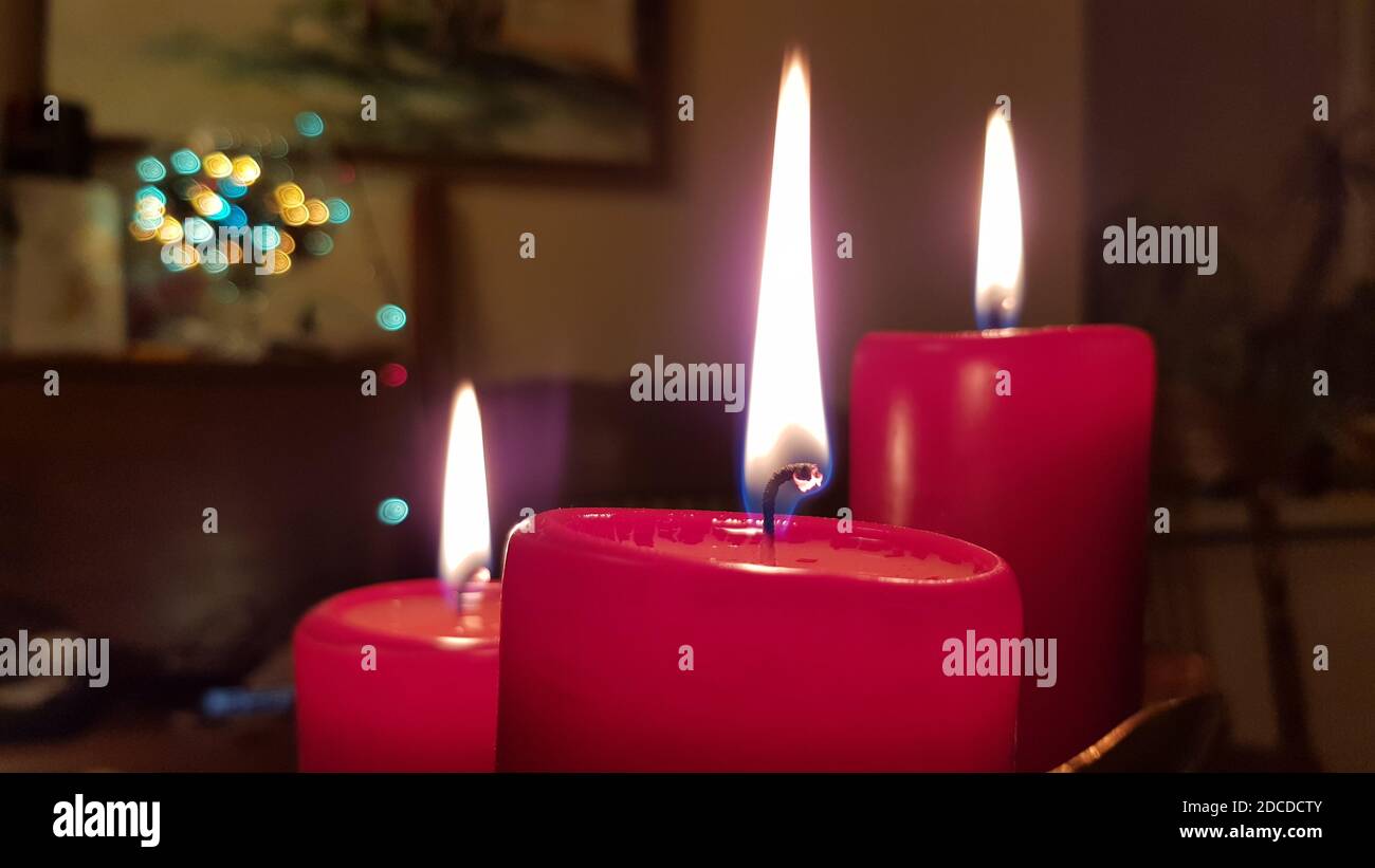 Red candles of different sizes. Candlelight flames on burning wickes closeup. Glowing fire of red candlesticks in darkness. Christmas candles closeup Stock Photo