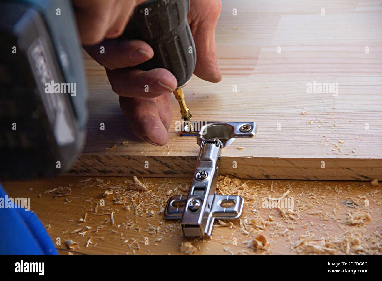 A man using an electric hand drill for work with a timber board, holes