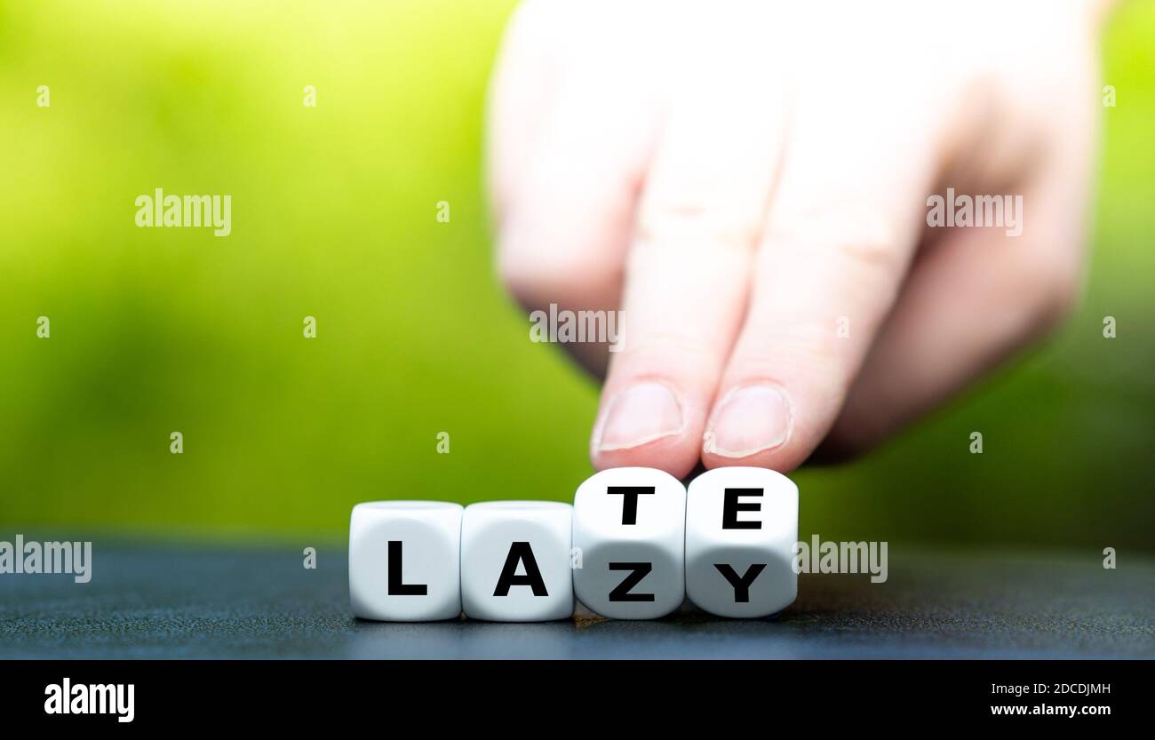 Hand turns dice and changes the word 'lazy' to 'late'. Stock Photo