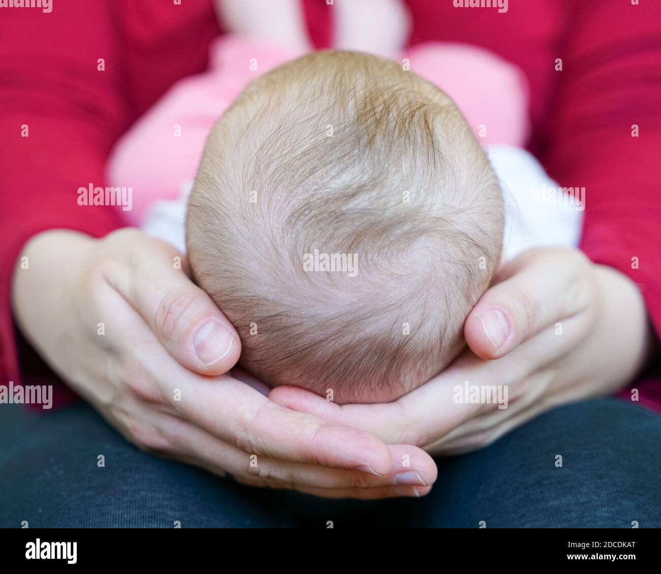 Mother lovingly holding newborn baby girl on her lap with its head in her hands and tiny feet touching her belly Stock Photo